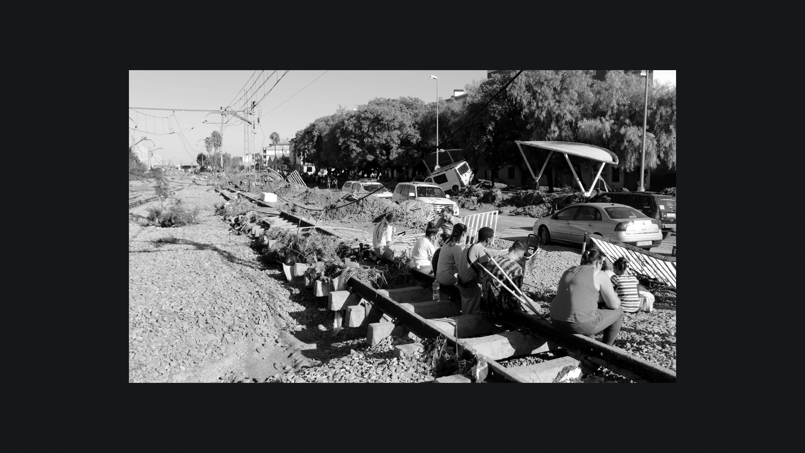 A la imatge, unes persones s'asseuen a sobre de la via del tren destrossada entre Picanya i Paiporta.